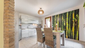A modern kitchen with white cabinets, a dining area with wicker chairs, and a bamboo forest mural on the wall. - Villa Camelia panoramic villa facing the sea (Torre Delle Stelle (Maracalagonis))