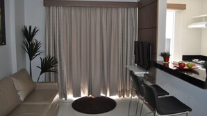 Ein Wohnzimmer mit einer Couch, einem Fernseher, einem Essbereich mit Stühlen und einem Fenster mit Vorhängen.