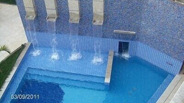 Ein Pool mit Wasserfall, umgeben von einer Fliesenwand.