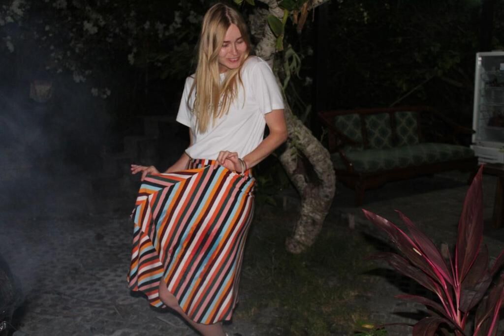 A person standing outdoors at night, wearing a white t-shirt and a striped skirt.