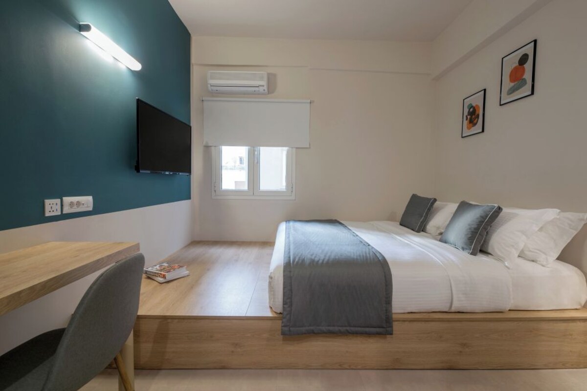 A compact bedroom with a bed, bedside table, chair, and a TV mounted on the wall.