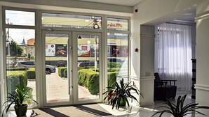 Un hall d’hôtel avec une entrée dotée d’une porte en verre, des plantes en pot, un comptoir de réception et une vue sur la rue.