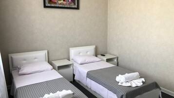 Een hotelkamer met twee éénpersoonsbedden, witte hoofdborden en een klein nachtkastje met een afstandsbediening.