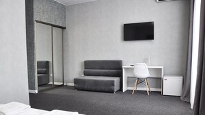 Une chambre d’hôtel comprenant un lit, un canapé gris, un bureau avec une chaise, un téléviseur à écran plat et un petit réfrigérateur.
