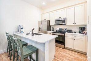 Una cocina moderna con armarios blancos, electrodomésticos de acero inoxidable, una isla central con taburetes y un microondas integrado.