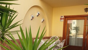 Un bâtiment jaune doté d’un balcon, une porte avec un panneau d’avertissement et des places assises à l’extérieur.