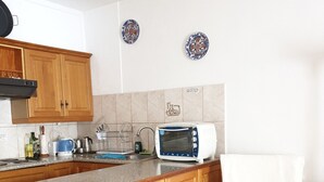 Une cuisine avec des meubles de rangement en bois, un four à micro-ondes, une bouilloire et une chaise dotée d’un coussin blanc.