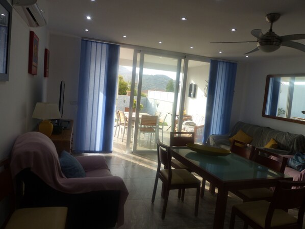 A living room with a sofa, a dining table with chairs, a ceiling fan, and a sliding glass door leading to an outdoor patio.