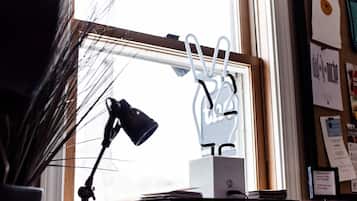 A desk with a lamp, a white box, and a window with a view of the outside.