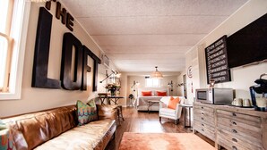 A cozy living room with a leather sofa, a dining table, and a kitchen area with a microwave and coffee maker.