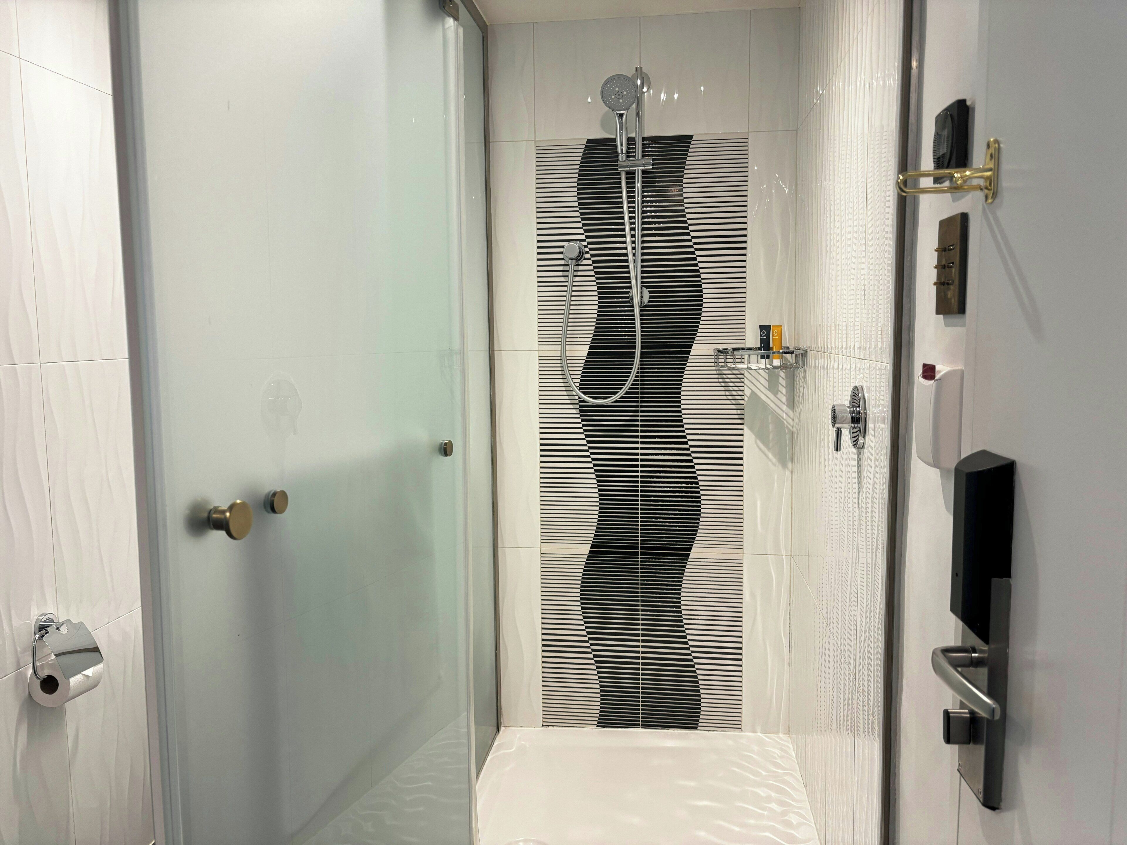 Un baño moderno con ducha, dispensador de papel higiénico y perchero para toallas.