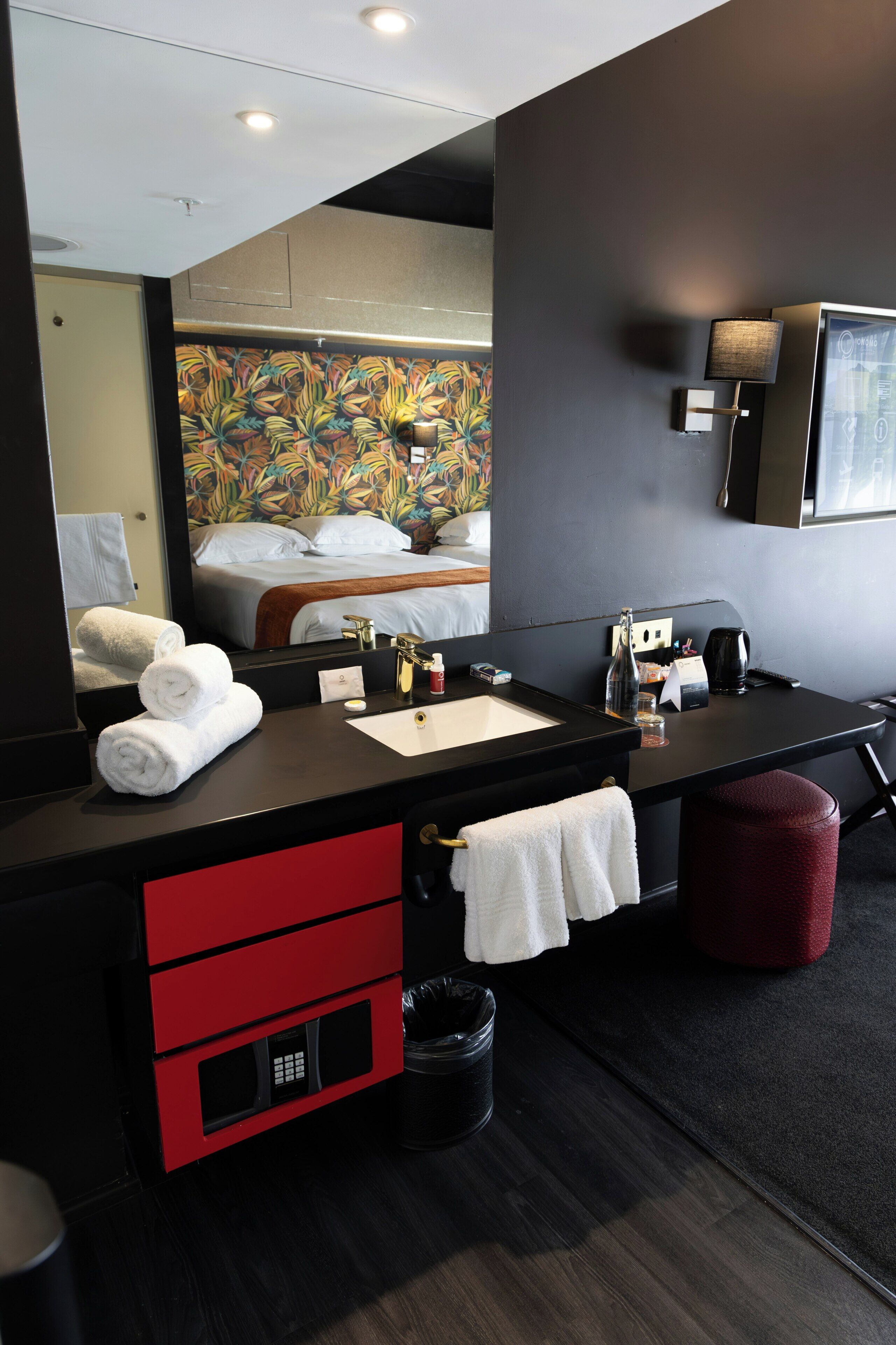 Un baño moderno con un espejo grande, un lavamanos, un mueble rojo y un cubo de basura negro.