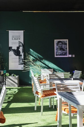 Un espacio al aire libre con sillas y mesas blancas, una pared verde y un cartel de un fotógrafo.