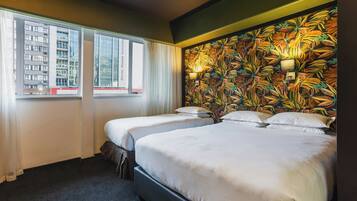 A hotel room with two beds, a window with curtains, and a wall with a tropical leaf pattern.