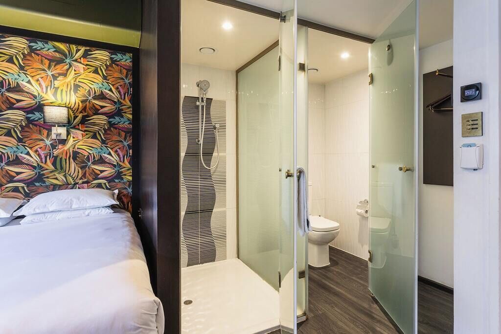 Habitación de hotel con cama, zona de ducha y un inodoro.