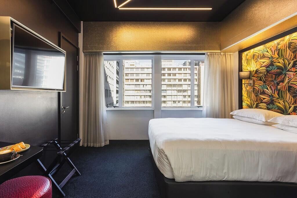 A hotel room with a bed, a desk, a chair, a TV, and a window with curtains.