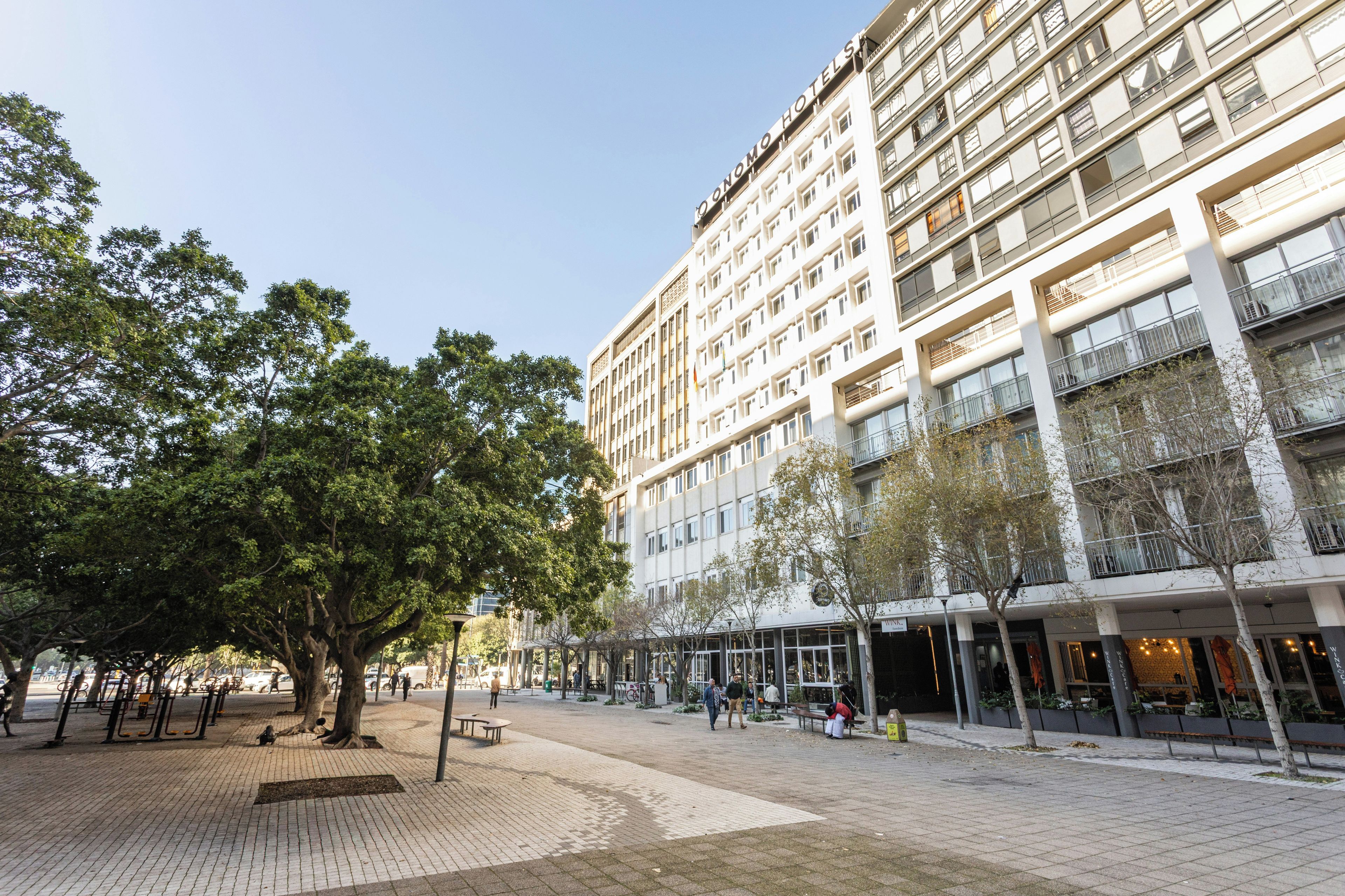 Un hotel con varios pisos, terraza exterior y árboles.