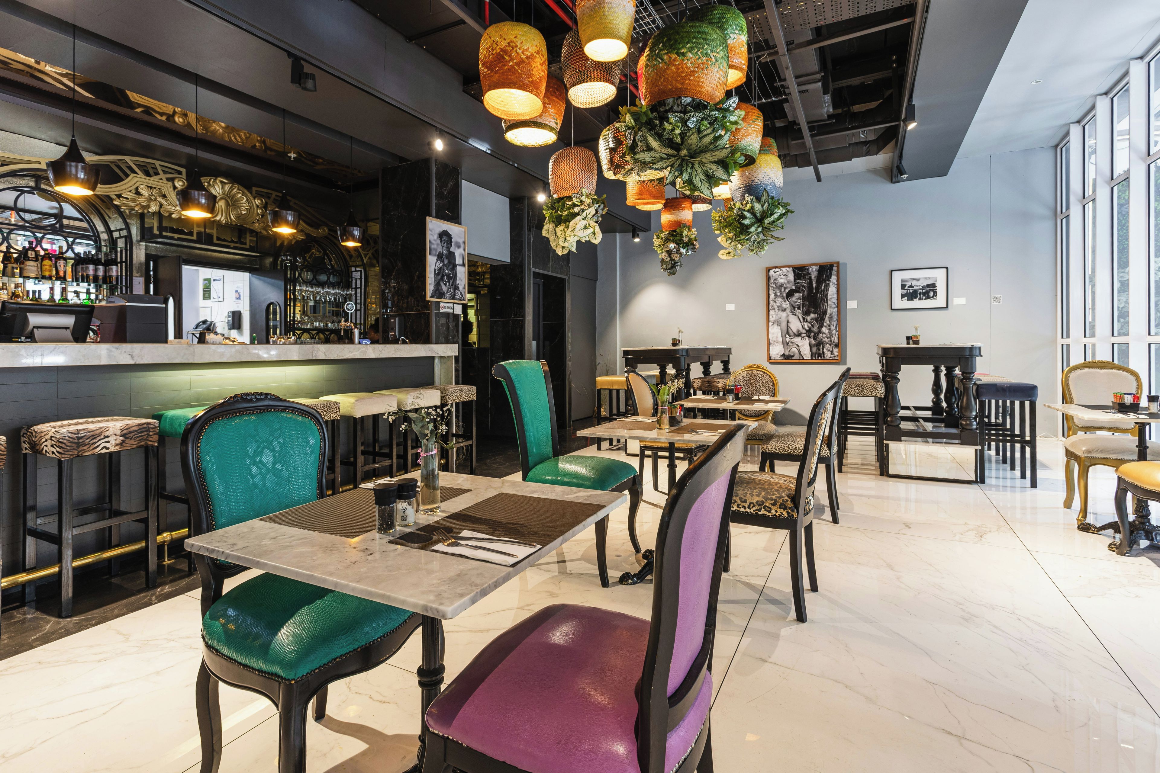 Interior de un restaurante con asientos de bar, mesas y luces decorativas colgantes.