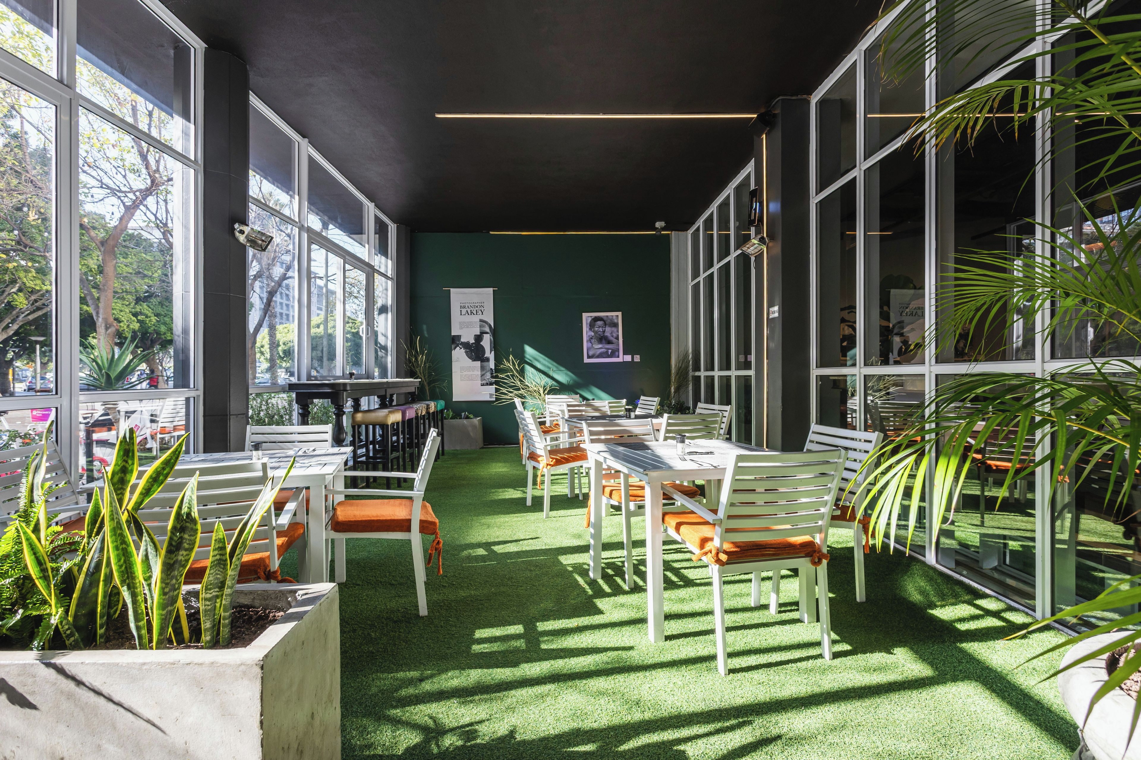 A modern indoor space with a green wall, large windows, and a seating area with white chairs and orange cushions.