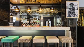 Uma área de bar com bancada de mármore, diversas garrafas de bebidas alcoólicas e vários banquetas.