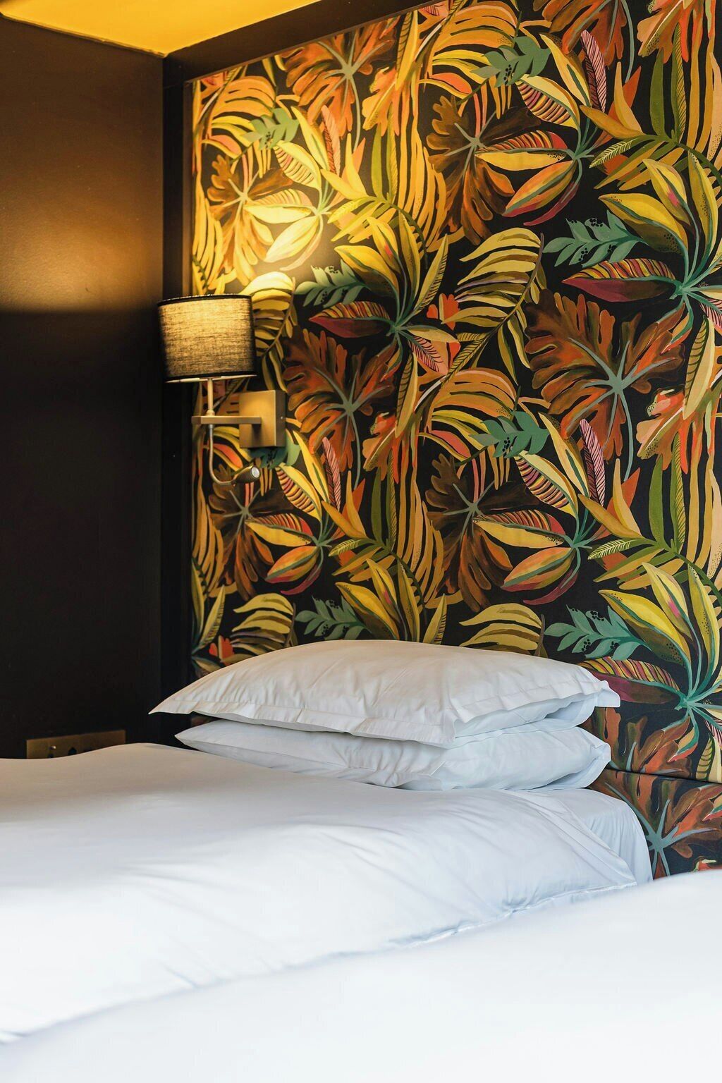 A hotel room with a bed, white bedding, and a wall with a tropical leaf pattern.