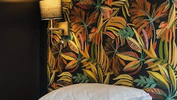 Una habitación de hotel con una cama, ropa de cama blanca y una pared con motivos de hojas tropicales.
