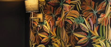 A hotel room with a bed, white bedding, and a wall with a tropical leaf pattern.