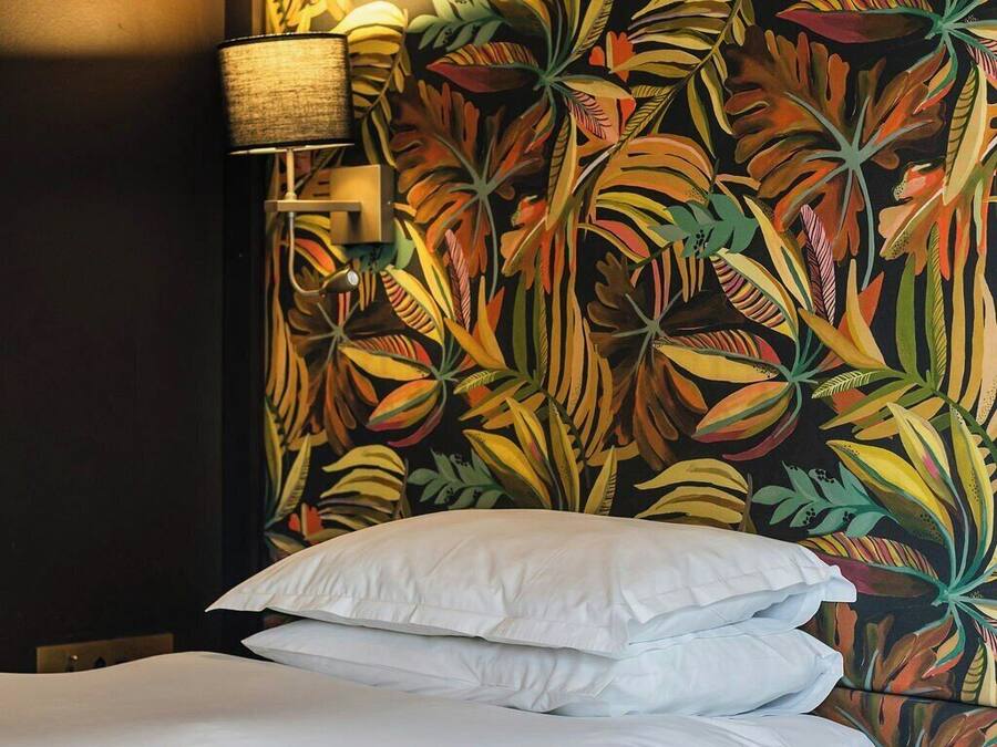 A hotel room with a bed, white bedding, and a wall with a tropical leaf pattern.