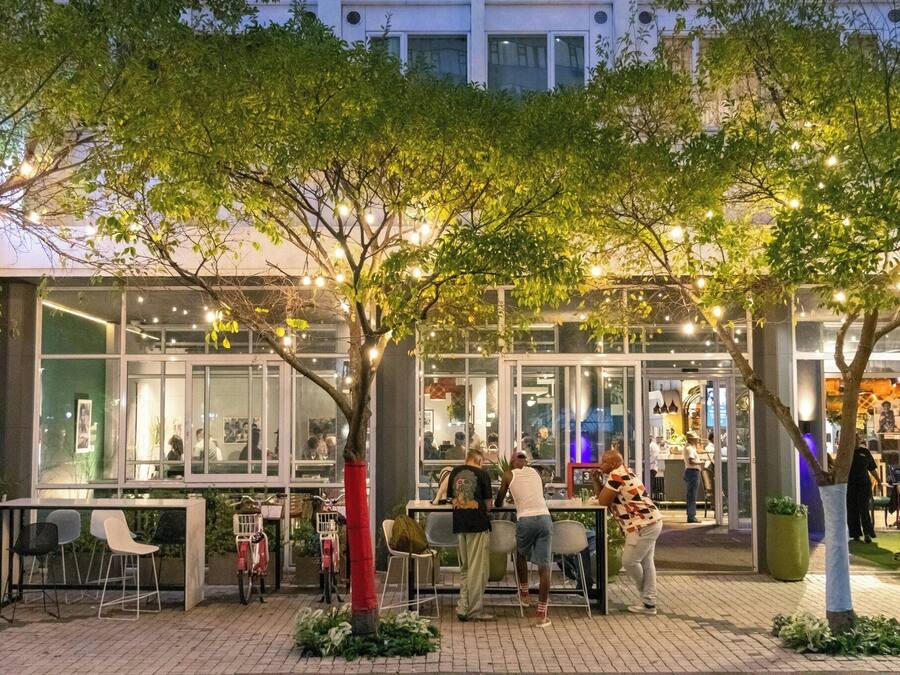 Un espacio al aire libre con mesas y sillas, rodeado de árboles y luces colgantes.