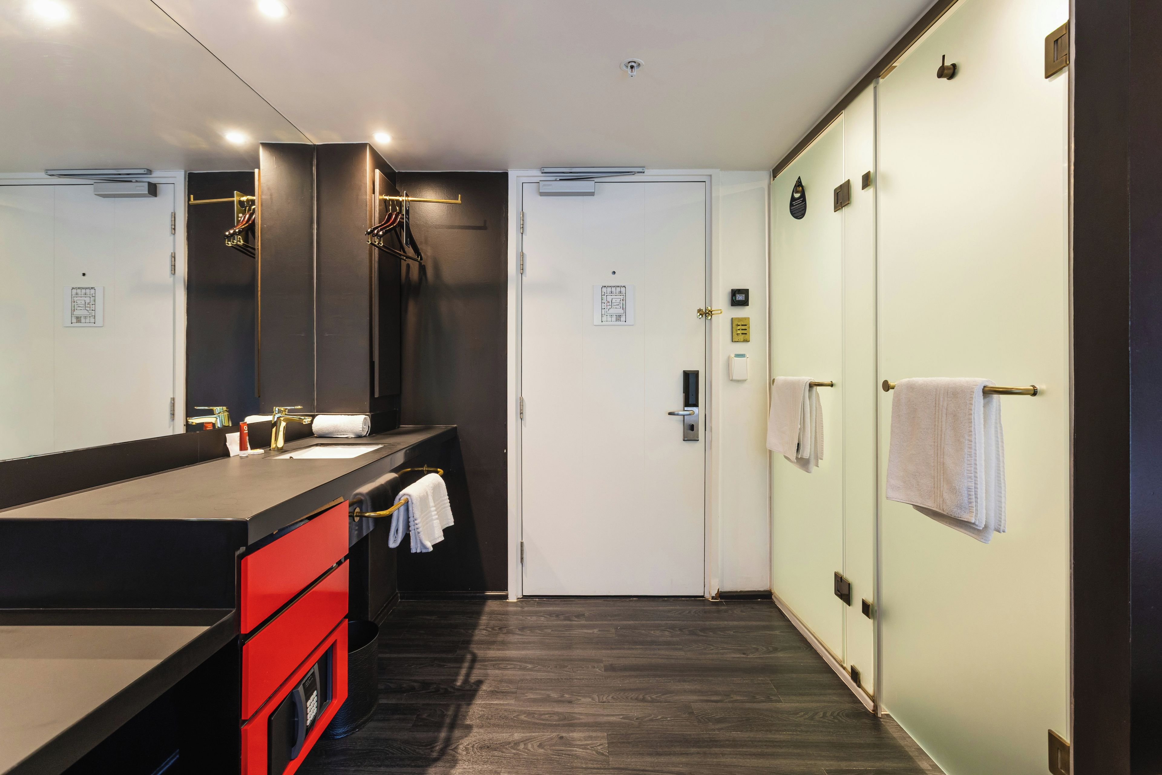 Une salle de bain moderne avec un plancher en bois foncé, un comptoir noir, un meuble rouge et un grand miroir.