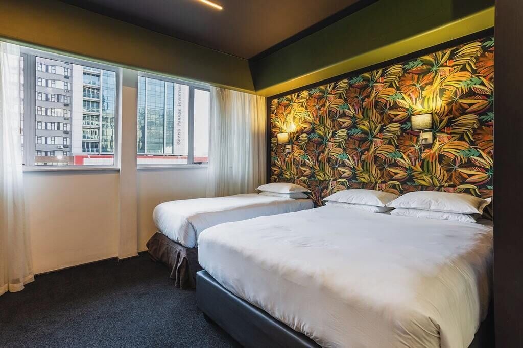 A hotel room with two beds, a large window, and a wall with a tropical leaf pattern.