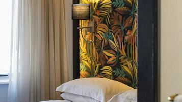 A hotel room with a bed, a window with curtains, and a wall with a tropical leaf pattern.