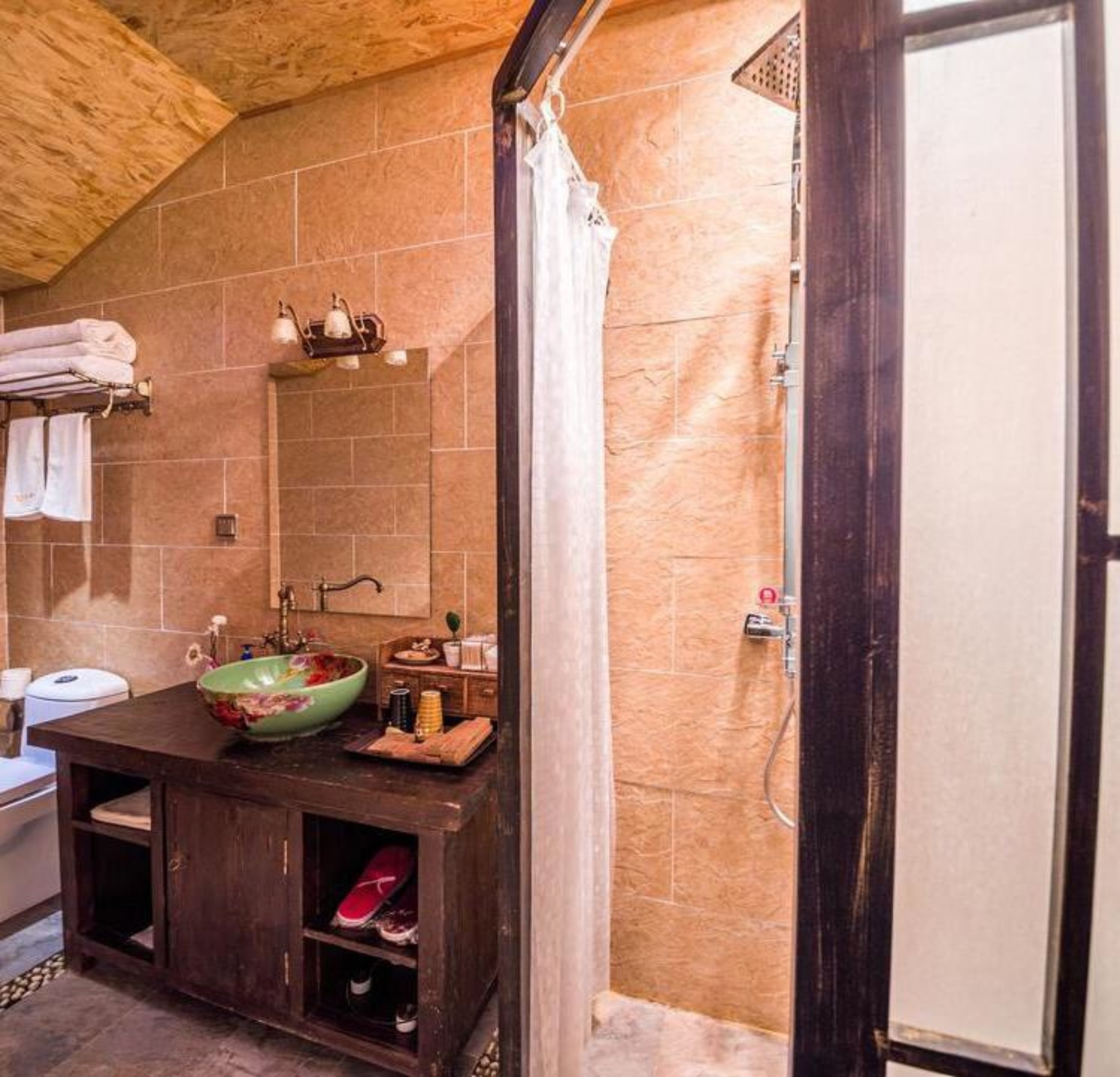 A bathroom with a wooden vanity, a green floral bowl sink, a mirror, and a shower area.