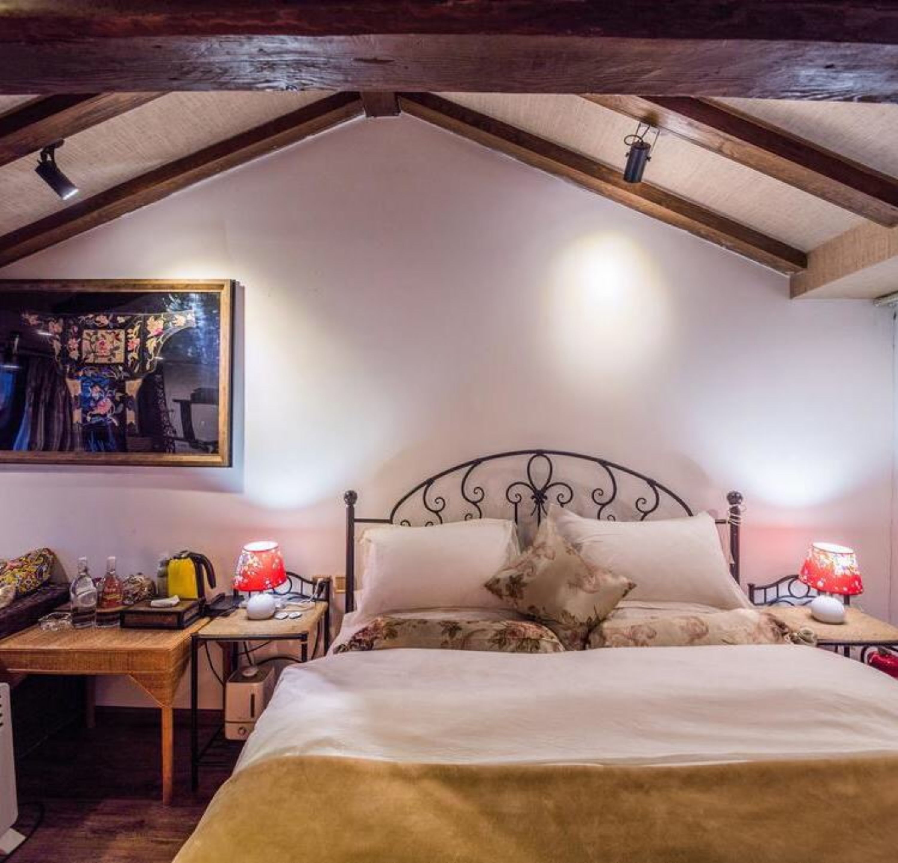 A bedroom with a sloped ceiling, a bed with floral bedding, two bedside tables with lamps, and a wall-mounted painting.