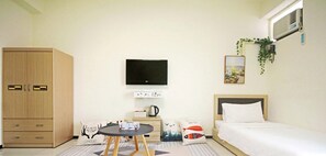 A hotel room with a bed, a TV, a wardrobe, a small table with a kettle, and a wall-mounted air conditioner.