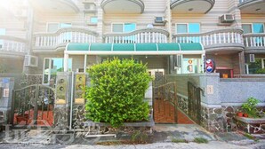 A multi-story residential building with balconies, a green awning over the entrance, and a small tree in front.