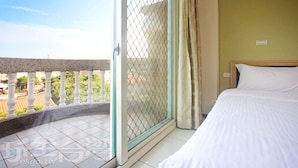 A hotel room with a bed, a window with a view of the outside, and a balcony with a railing.
