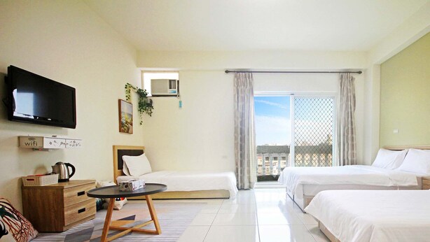 A hotel room with two beds, a television, a small table, a sofa, and a balcony with a view.