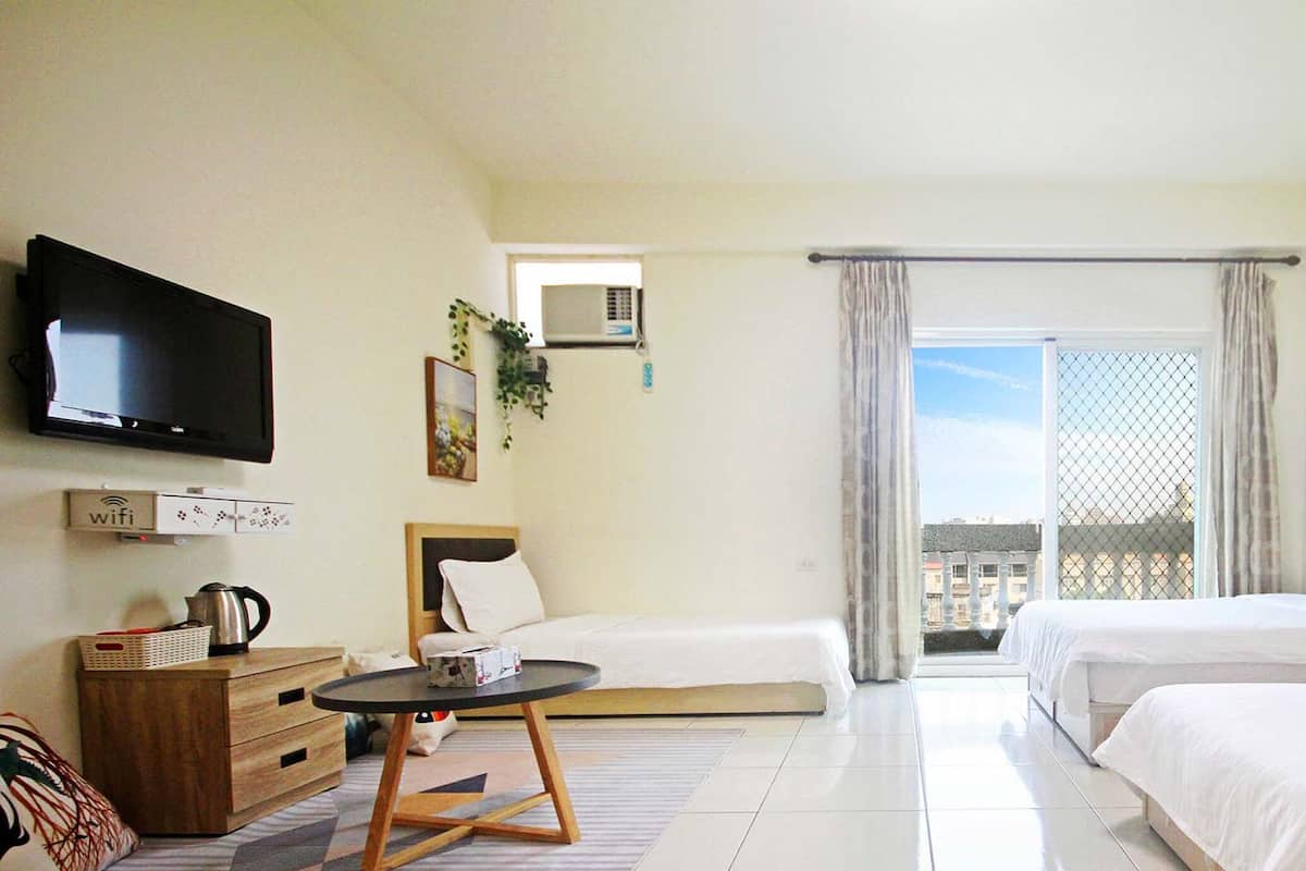 Habitación de hotel con dos camas, televisión, una mesita, sofá y balcón con vistas.
