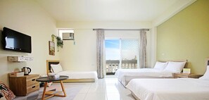 Ein Hotelzimmer mit zwei Betten, einem Fernseher, einem kleinen Tisch, einer Couch und einem Balkon mit Blick.