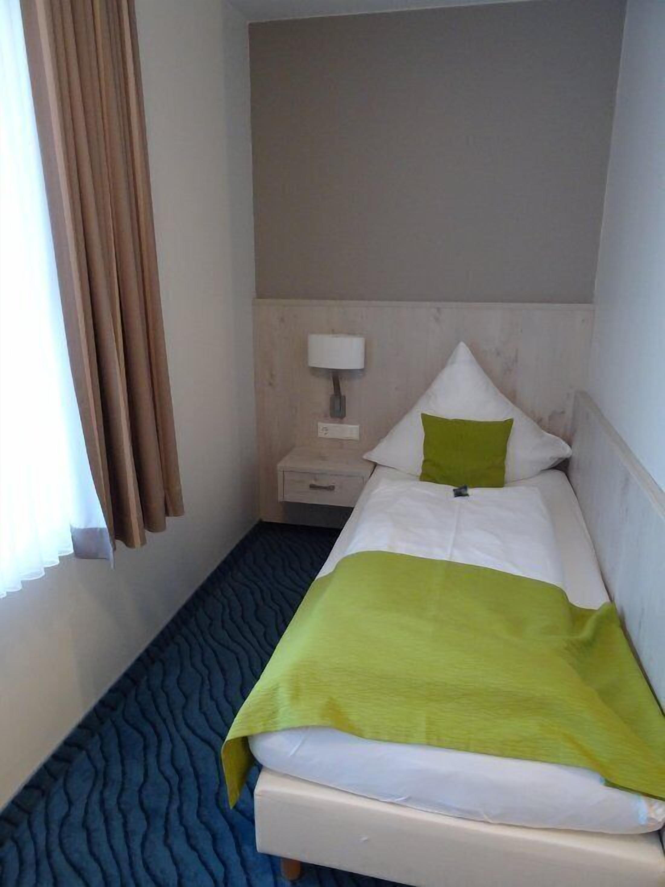 Ein Hotelzimmer mit einem Bett, einem Nachttisch, einer Lampe und einem Fenster mit Vorhängen.