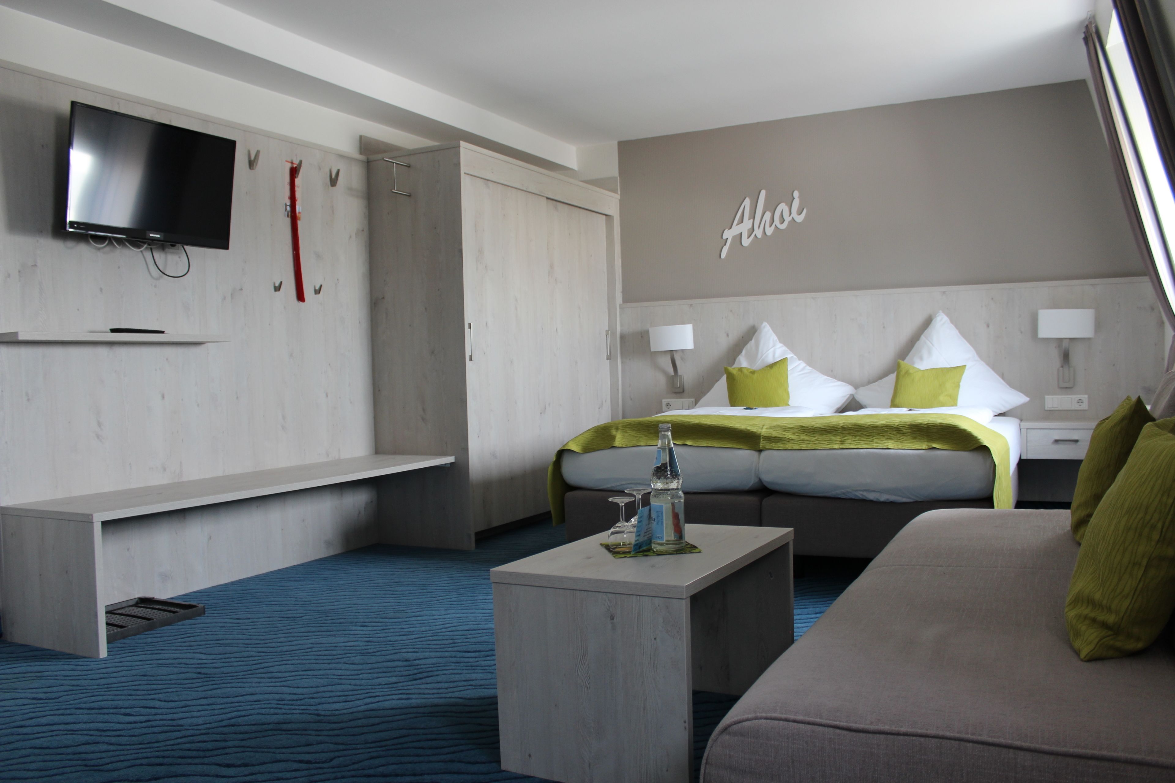 Ein modernes Hotelzimmer mit einem Bett, einer Couch, einem an der Wand montierten Fernseher und einem Nachttisch mit einer Flasche und Gläsern.