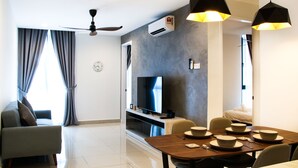 A modern living room with a flat-screen TV, a dining table set for four, and a ceiling fan. - H2O Residences by Victoria Home (Petaling Jaya)