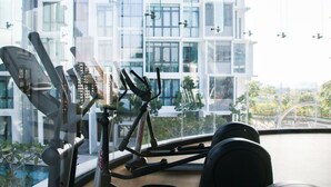 A gym with exercise equipment and a view of a modern building with balconies. - H2O Residences by Victoria Home (Petaling Jaya)