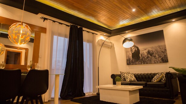 A living room with a wooden ceiling, a black sofa with patterned cushions, a white coffee table, and a globe chandelier.