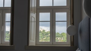 A room with two windows, one of which is open, revealing a view of a building and greenery outside. - O Paço - Exclusive Accommodation (Tomar)