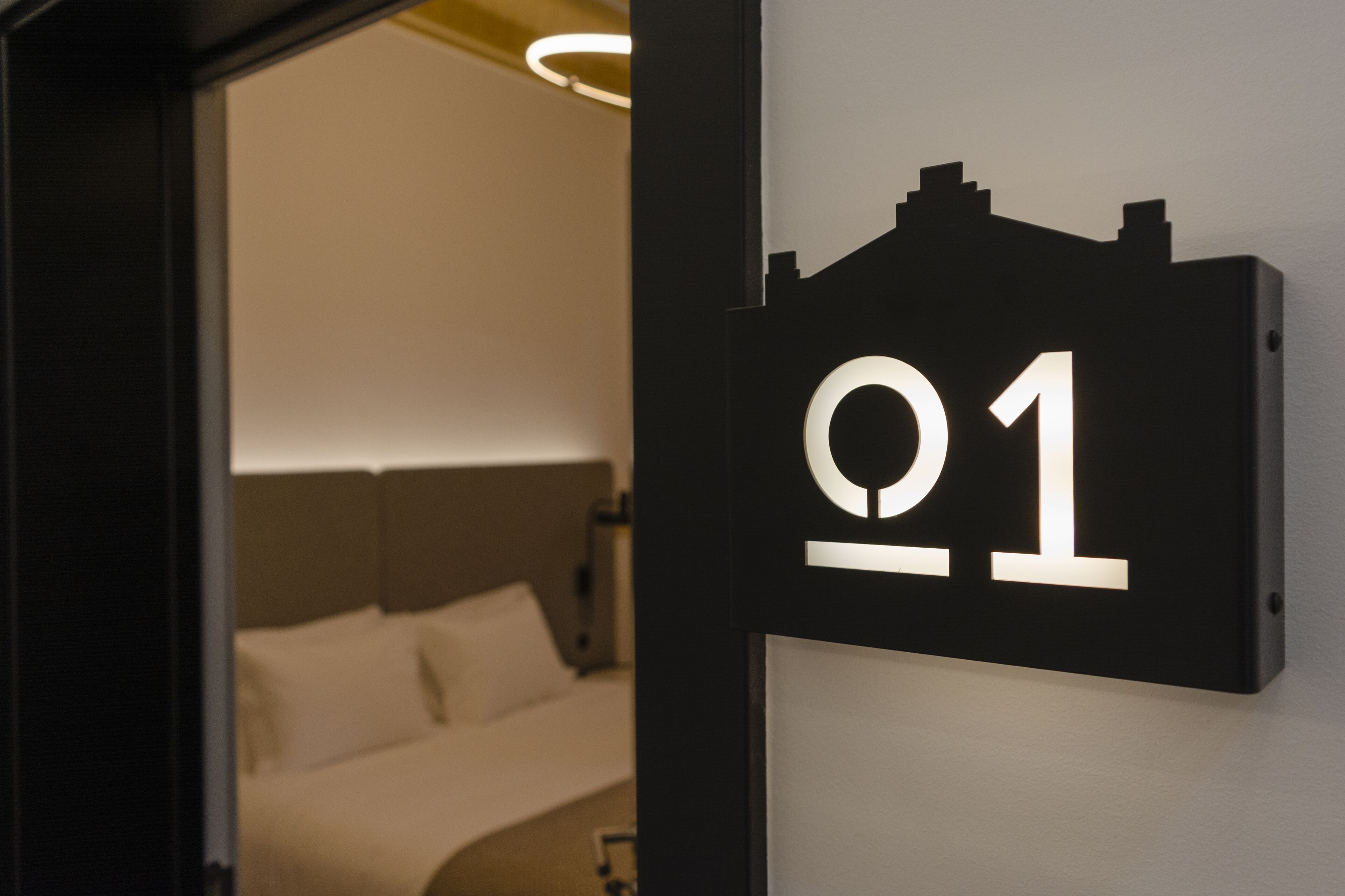 Ett hotellrum med en säng, en sänggavel och en skylt som visar att det är rum nummer 01.