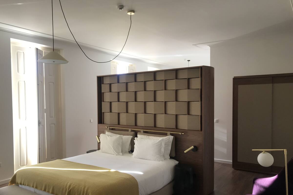 Un dormitorio moderno con una cama grande, un cabecero con diseño geométrico, un banco al pie de la cama, una mesita de noche y un armario.