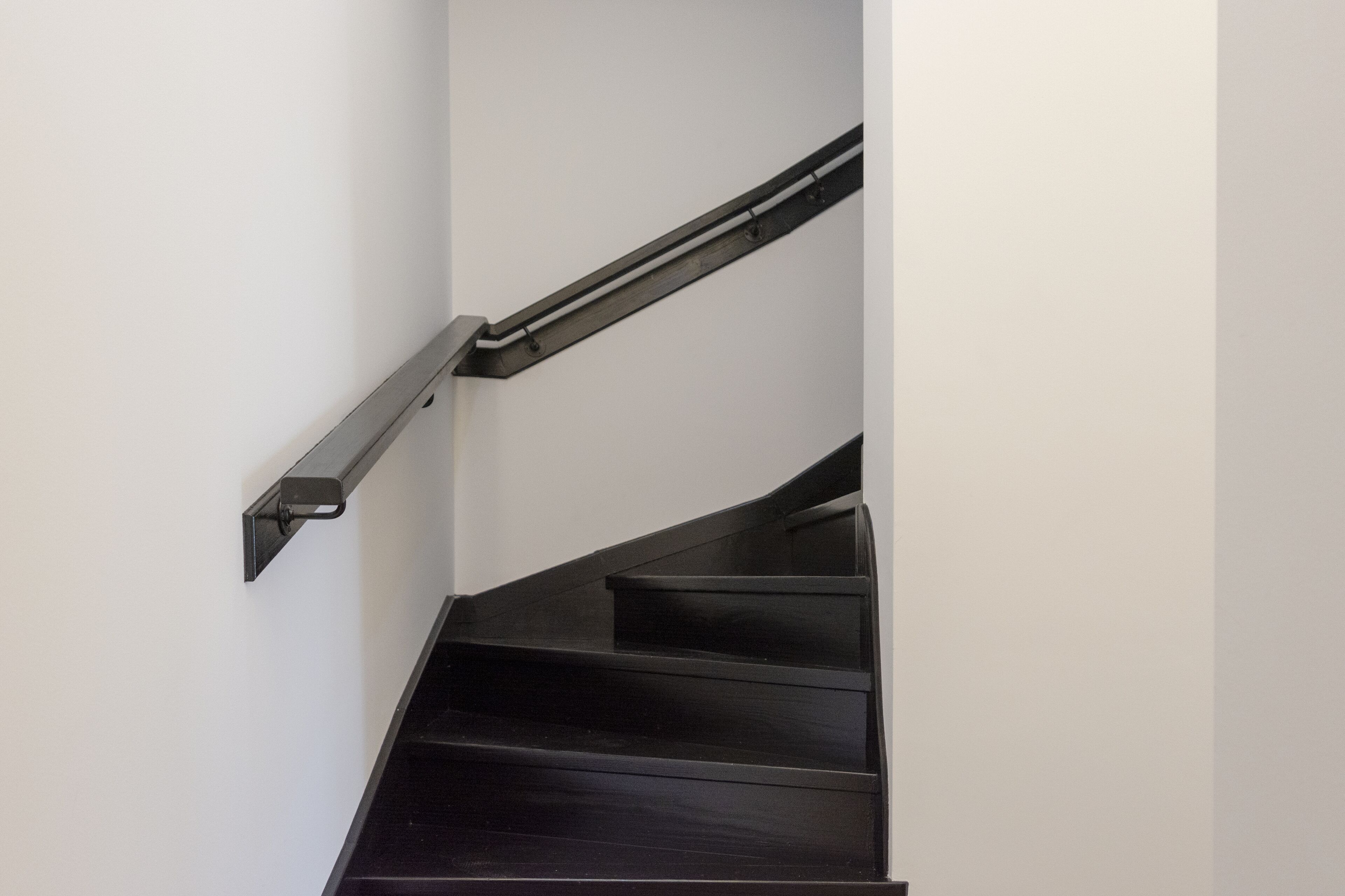 A black metal handrail and wooden steps of a staircase.