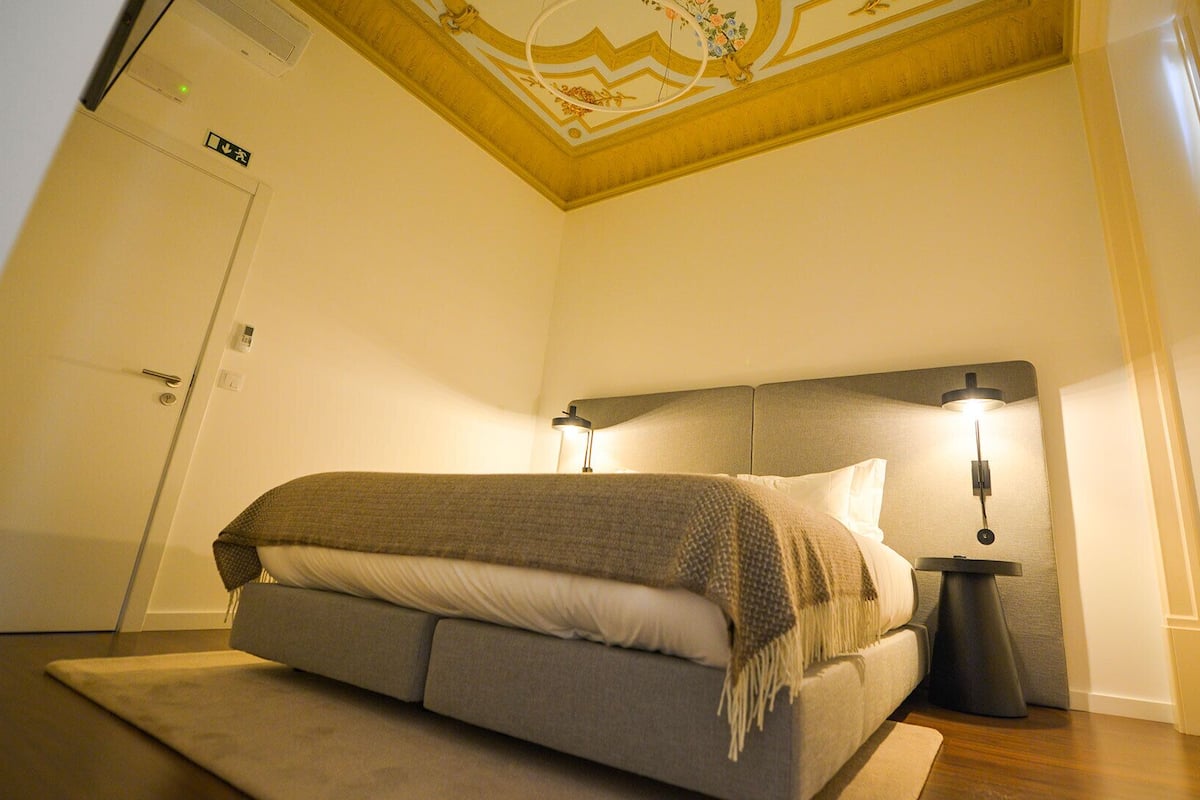 Un dormitorio con una cama, lámparas de noche, un techo con diseño decorativo y una puerta.